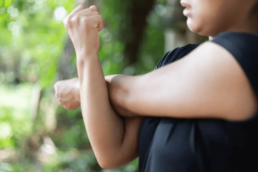 Mulher alongando realizando movimento de alongamento de braços.