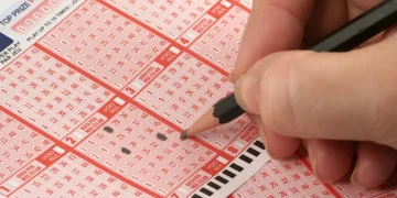 Person filling out a lottery ticket with a pencil.