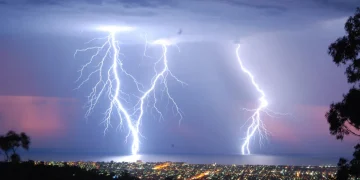 Lightning illuminating the night sky over a city and the ocean.