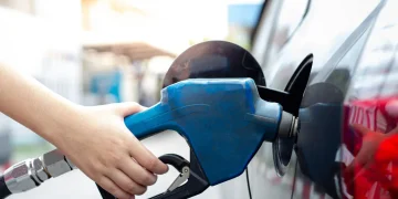 Hand holding a blue fuel pump nozzle in a car's gas tank.